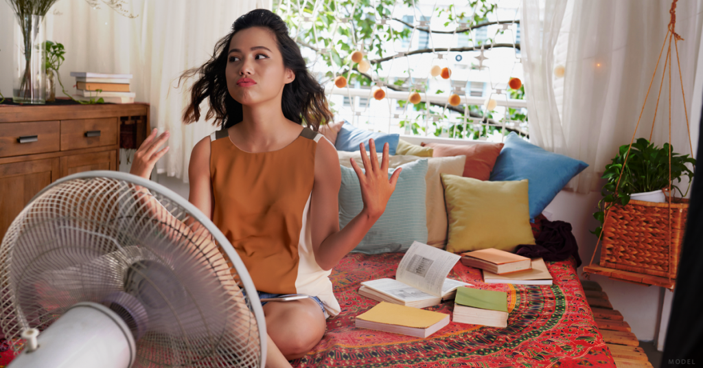 A woman experiencing hot flashes sits in front of an oscillating fan.