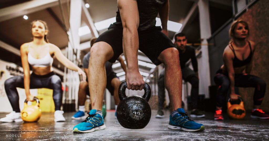 A group of people who use hormone therapy lift kettlebells in a workout class.