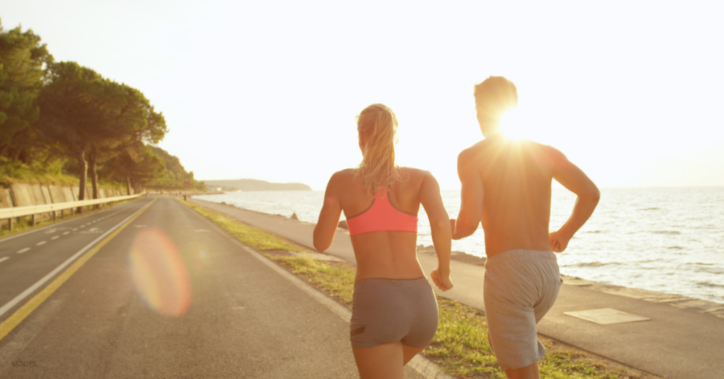 A woman and a man run on a road next to a river.