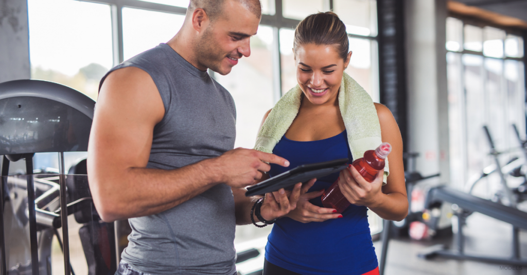 A man and a woman review their workout stats on a tablet.