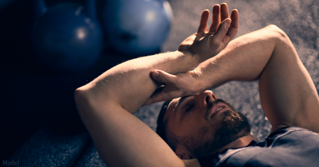 Exhausted man (model) resting in the gym by kettlebells with his hands over his head