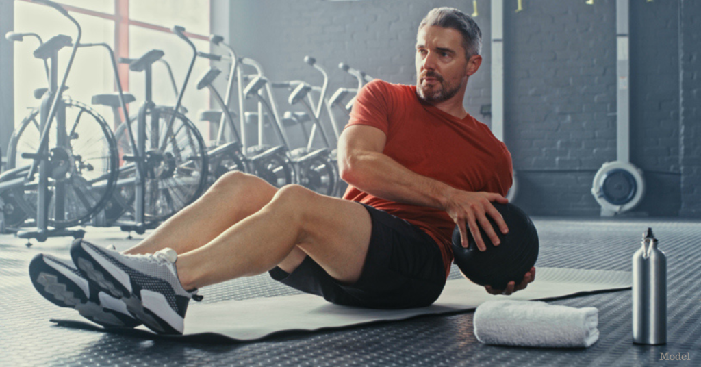 Man in the gym using a medicine ball, performing an oblique twist exercise (model)