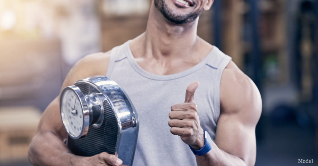 Closeup shot of a muscular man holding a scale and showing thumbs up in a gym (model)