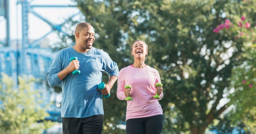 A couple outdoors in a city park, exercising together with weight smiling (models)